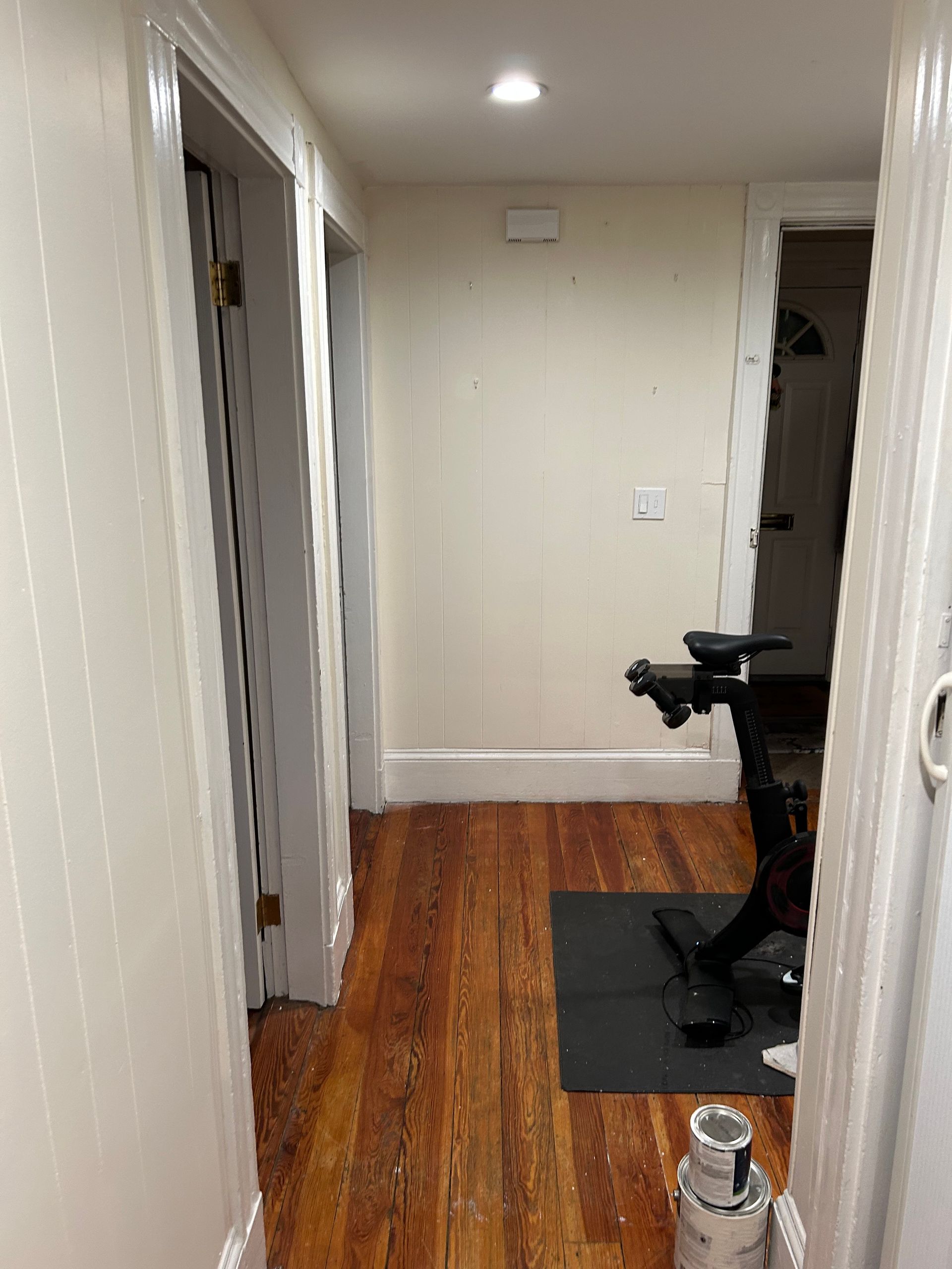 A hallway with wooden floors and white walls leading to a gym.