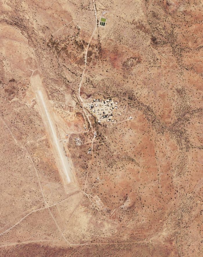 Aerial view of a small settlement in a desert landscape with an airstrip and scattered buildings.