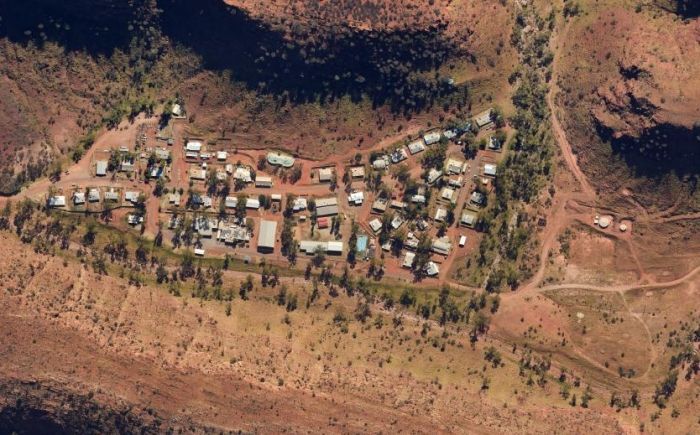 Aerial view of a small community nestled in a valley with red-brown hills and sparse vegetation.