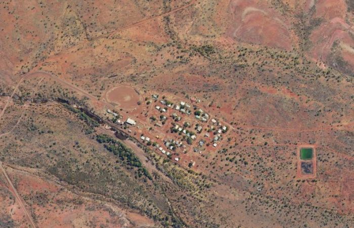 Aerial view of a small settlement in an arid landscape, with clustered buildings and two rectangular water tanks.