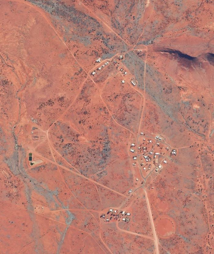 Aerial view of a small settlement in a reddish-brown desert landscape with dirt roads.