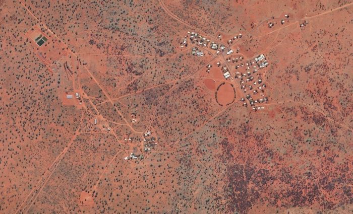Aerial view of a village in a reddish arid landscape with scattered buildings and a large circular feature.