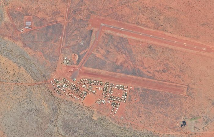 Aerial view of an outback airport with red runways, buildings, and a small town set in a reddish-brown landscape.