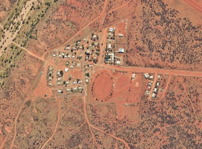 Aerial view of an outback Australian town with red dirt roads and houses. An oval-shaped space dominates the center.