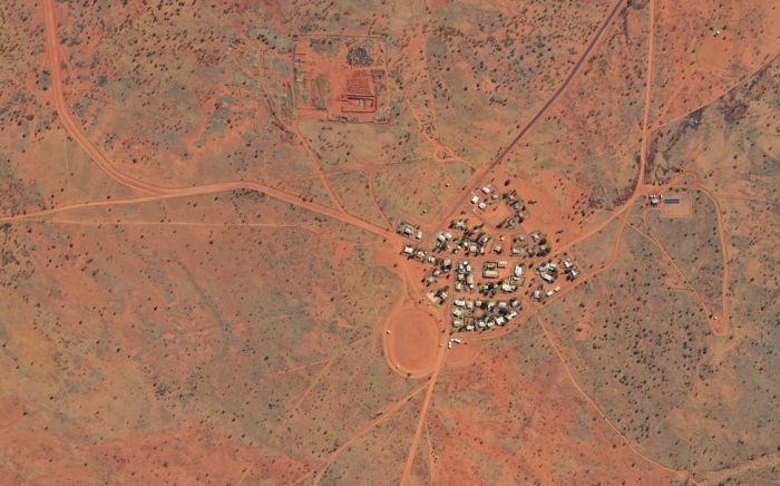 Aerial view of a small community with red dirt surroundings and connected by dirt roads in Australia.