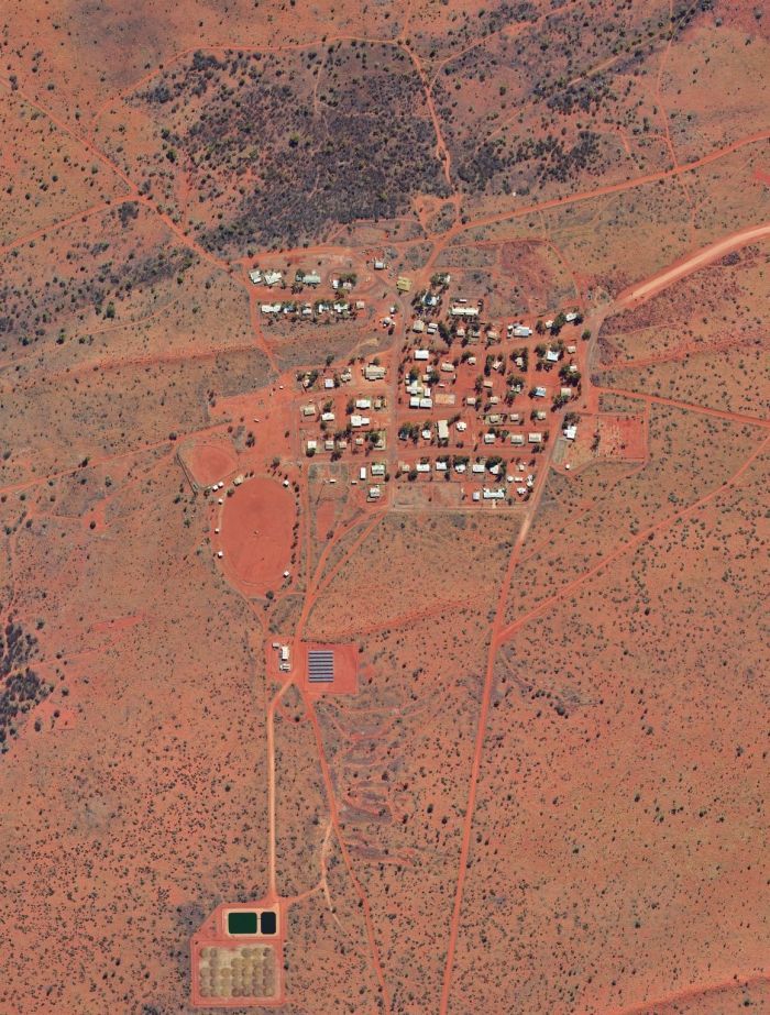 Aerial view of a small, scattered town in a red desert landscape. Roads and structures are visible.