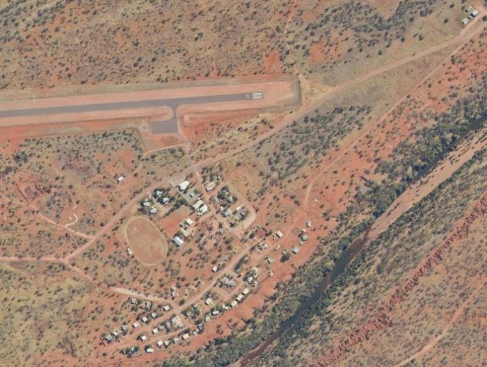 Aerial view of a small outback town next to a runway, with red earth and sparse vegetation.
