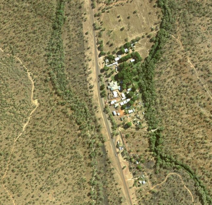 Aerial view of a small settlement nestled in a valley, surrounded by arid, brown hills and a meandering green river.