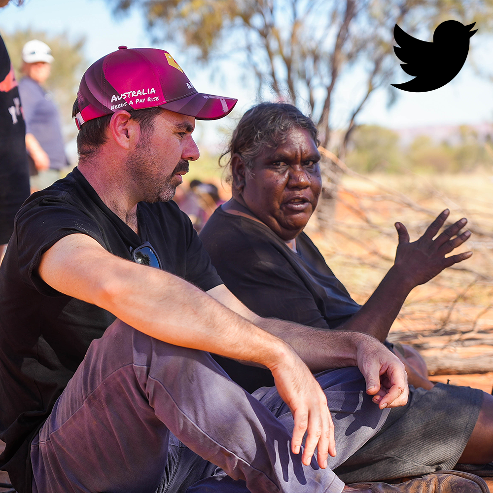 Man in cap and Indigenous woman seated outside, discussing, gesturing.