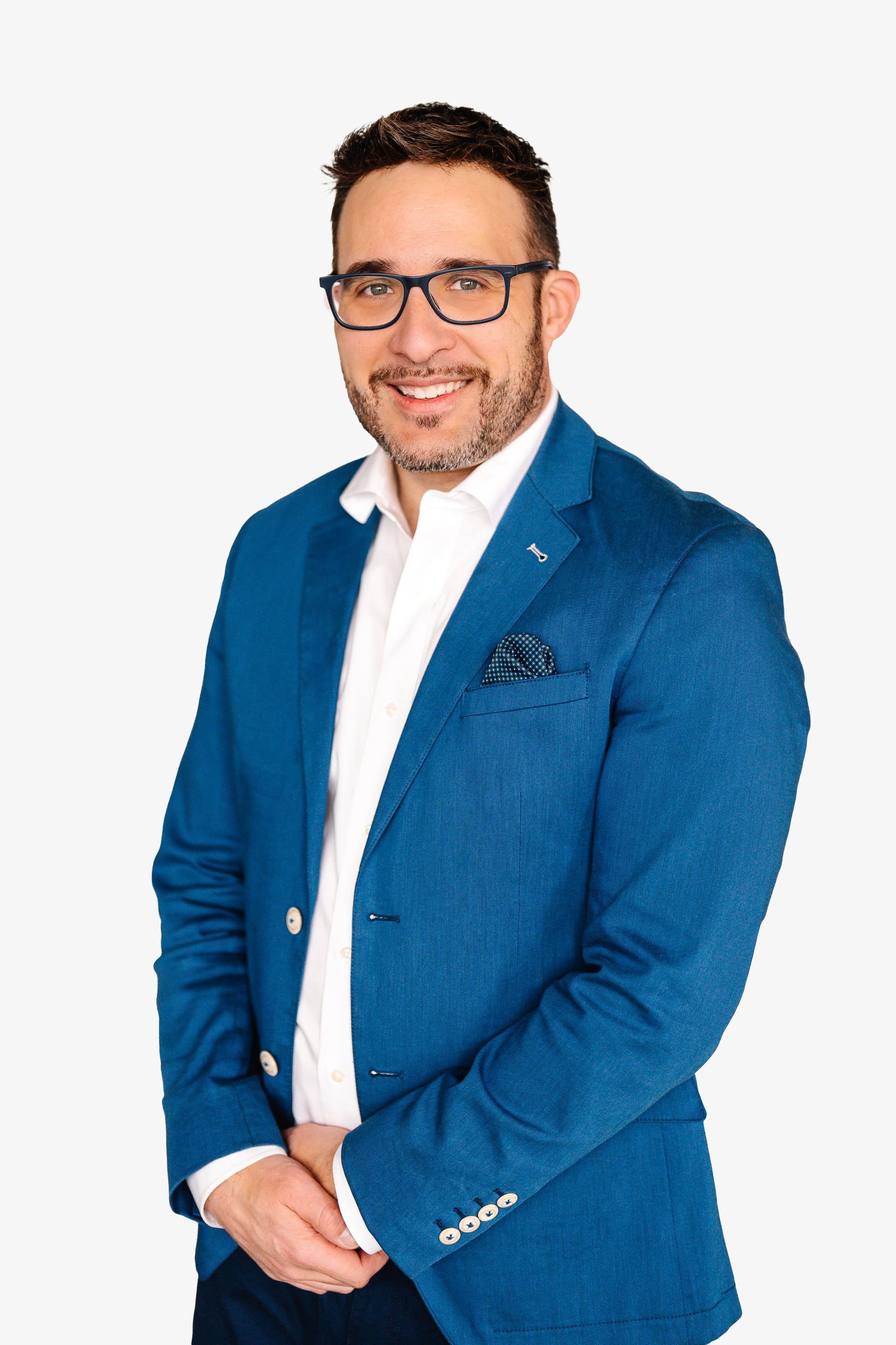 Un homme portant une veste bleue et des lunettes se tient devant un fond blanc.