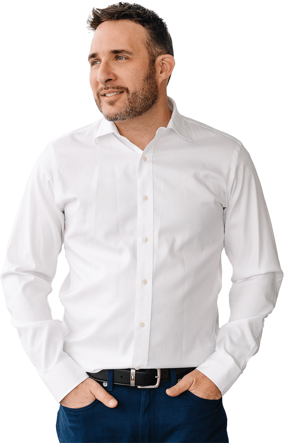 Un homme en chemise blanche et jean bleu est debout, les mains dans les poches.