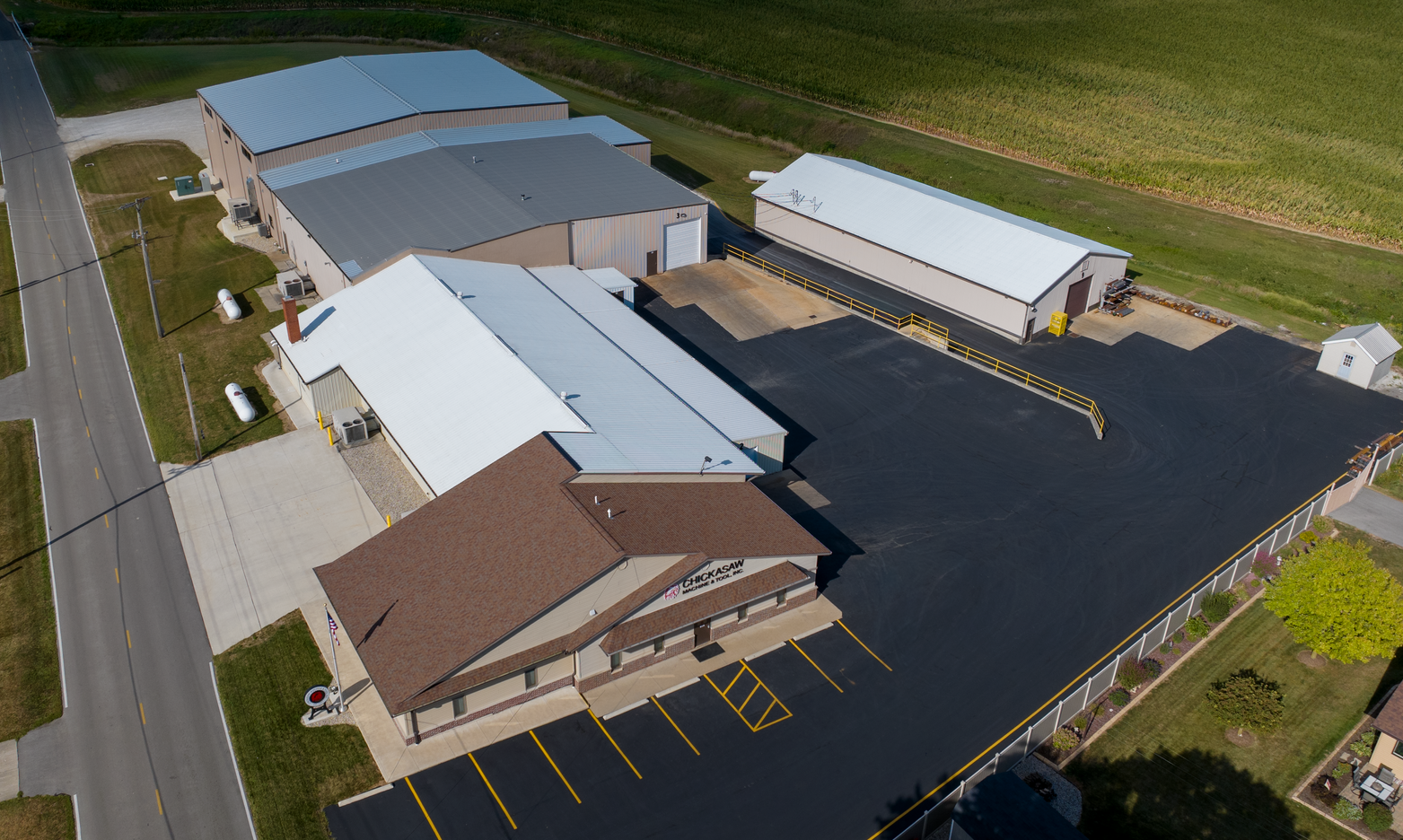 Aerial view of commercial buildings with black asphalt parking lot and surrounding greenery.