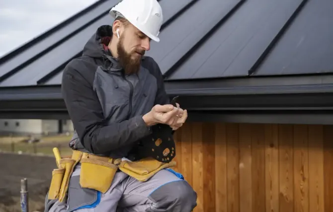 A man wearing a hard hat and headphones is sitting on the roof of a building.