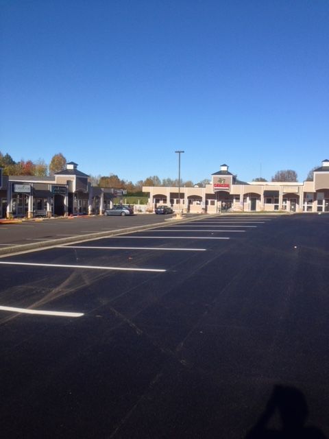 Empty parking lot in front of a one-story strip mall under a clear blue sky.