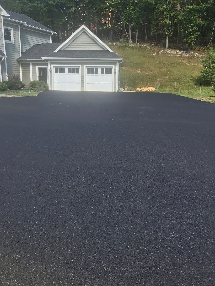 Newly paved black asphalt driveway leading to a two-car garage with white doors.