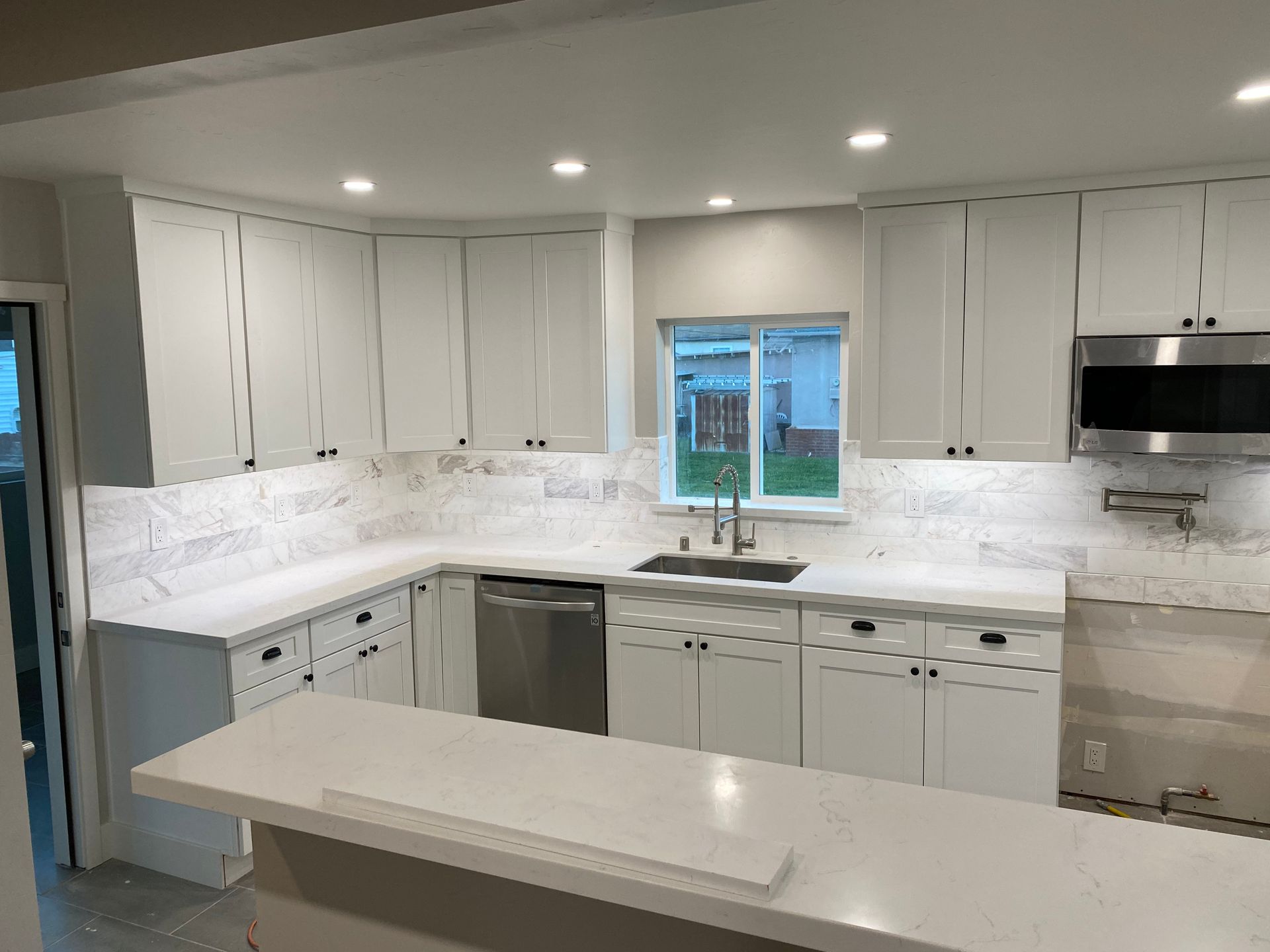 A kitchen with white cabinets , stainless steel appliances , a sink , and a window.