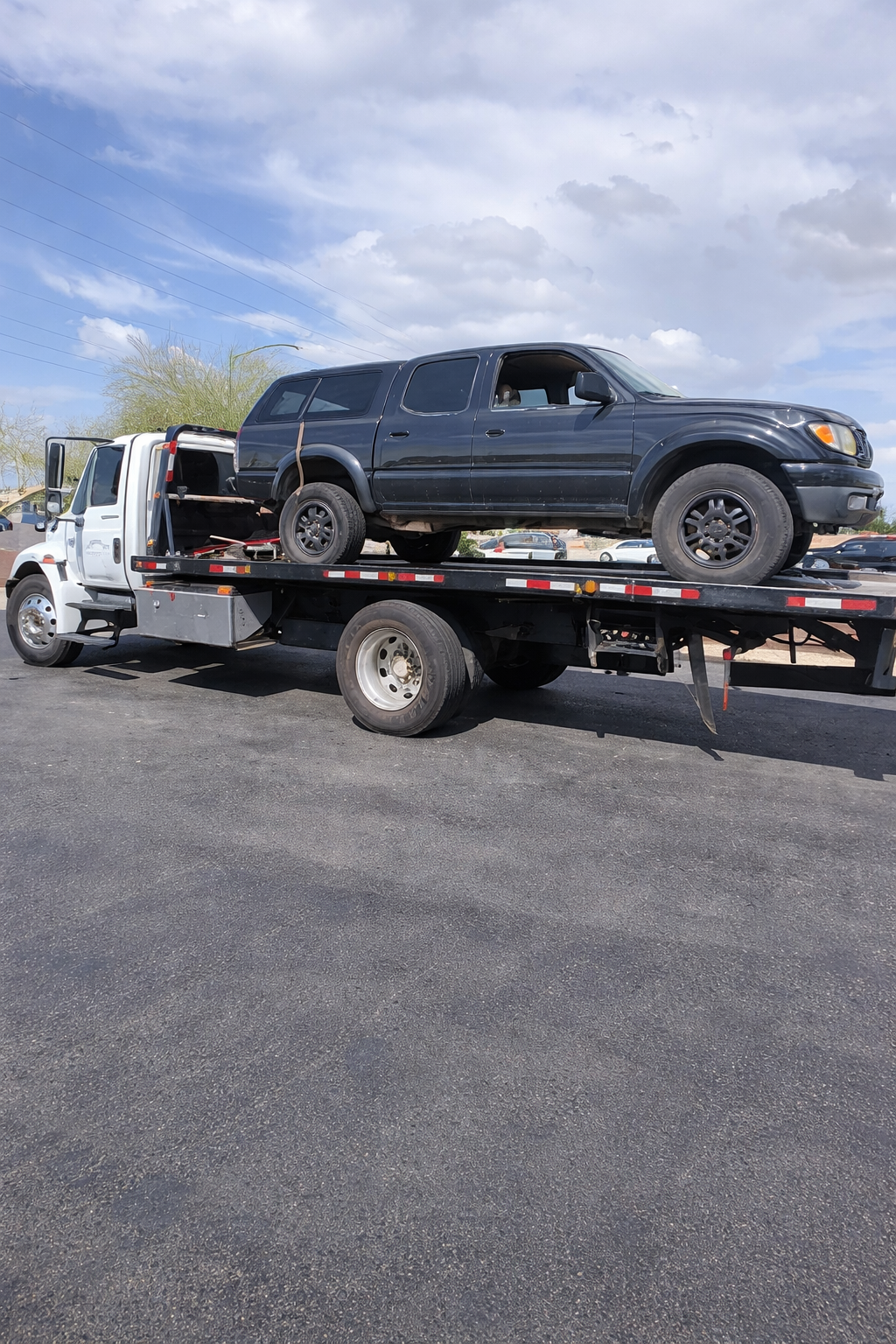 Dark gray truck on a white tow truck bed on a black asphalt lot under a blue sky.