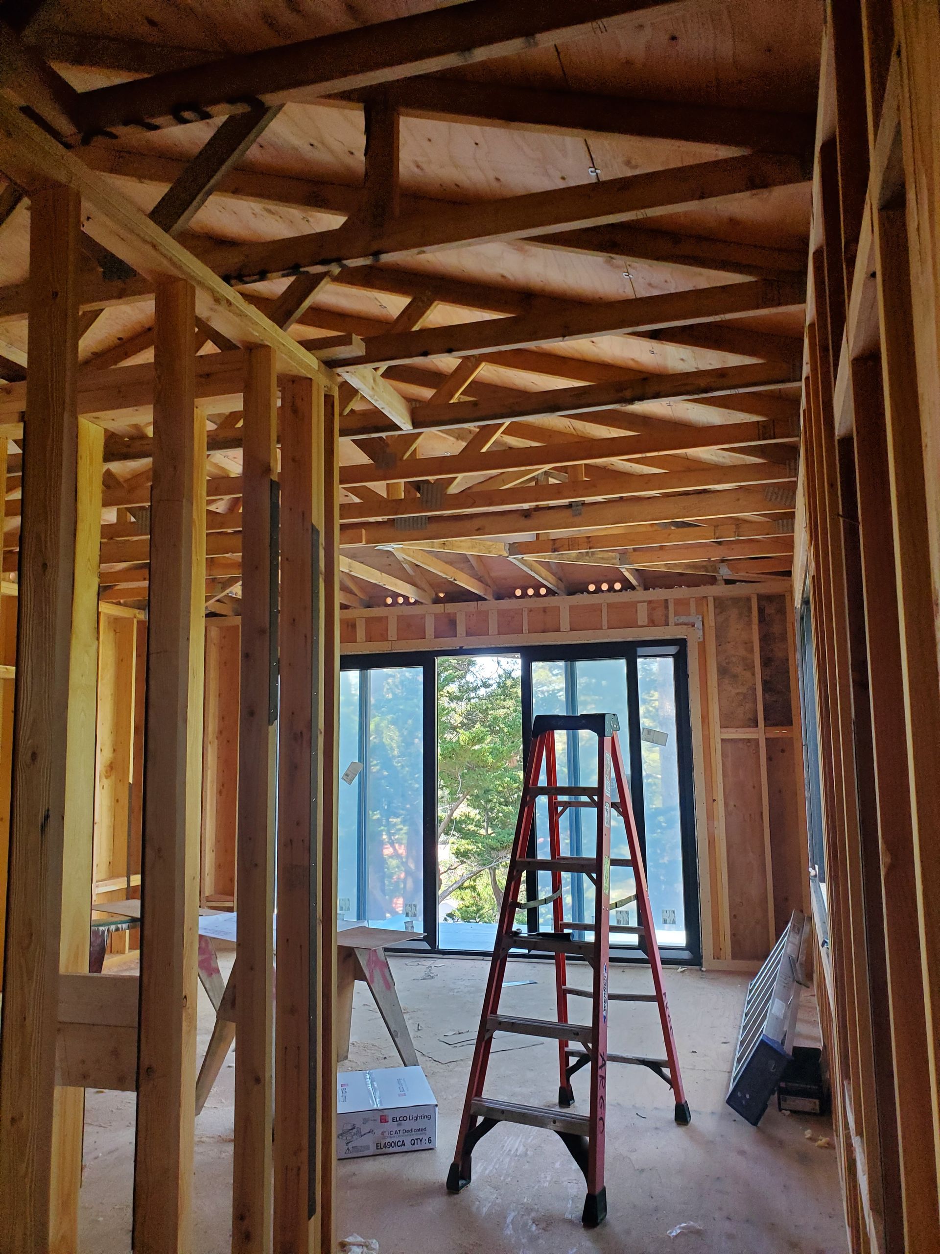 A worker stands in a kitchen under construction, surrounded by unfinished wooden cabinetry and workspace islands.