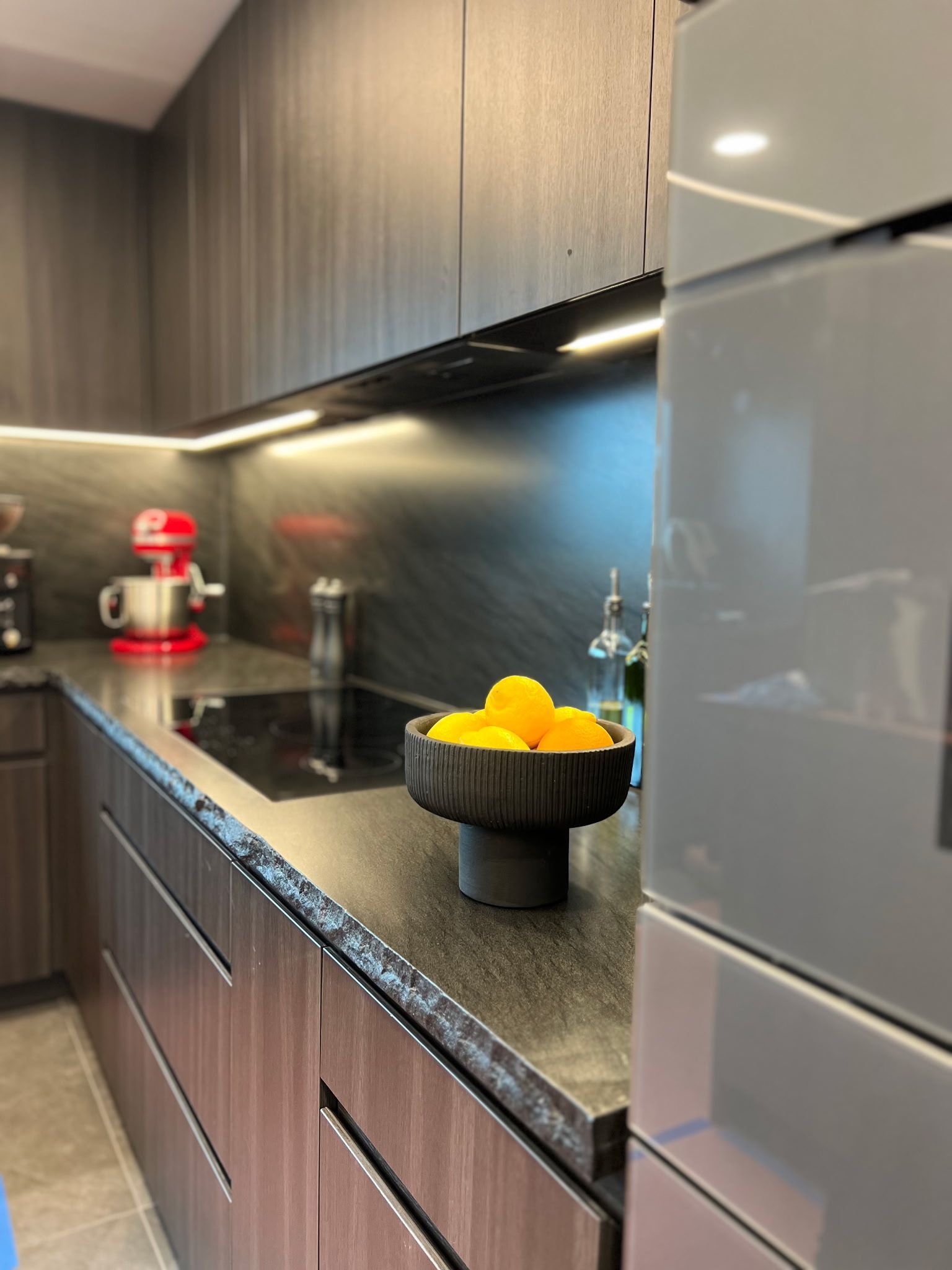 Modern kitchen with dark wood cabinets, a black countertop, a bowl of yellow lemons, and a red stand mixer.