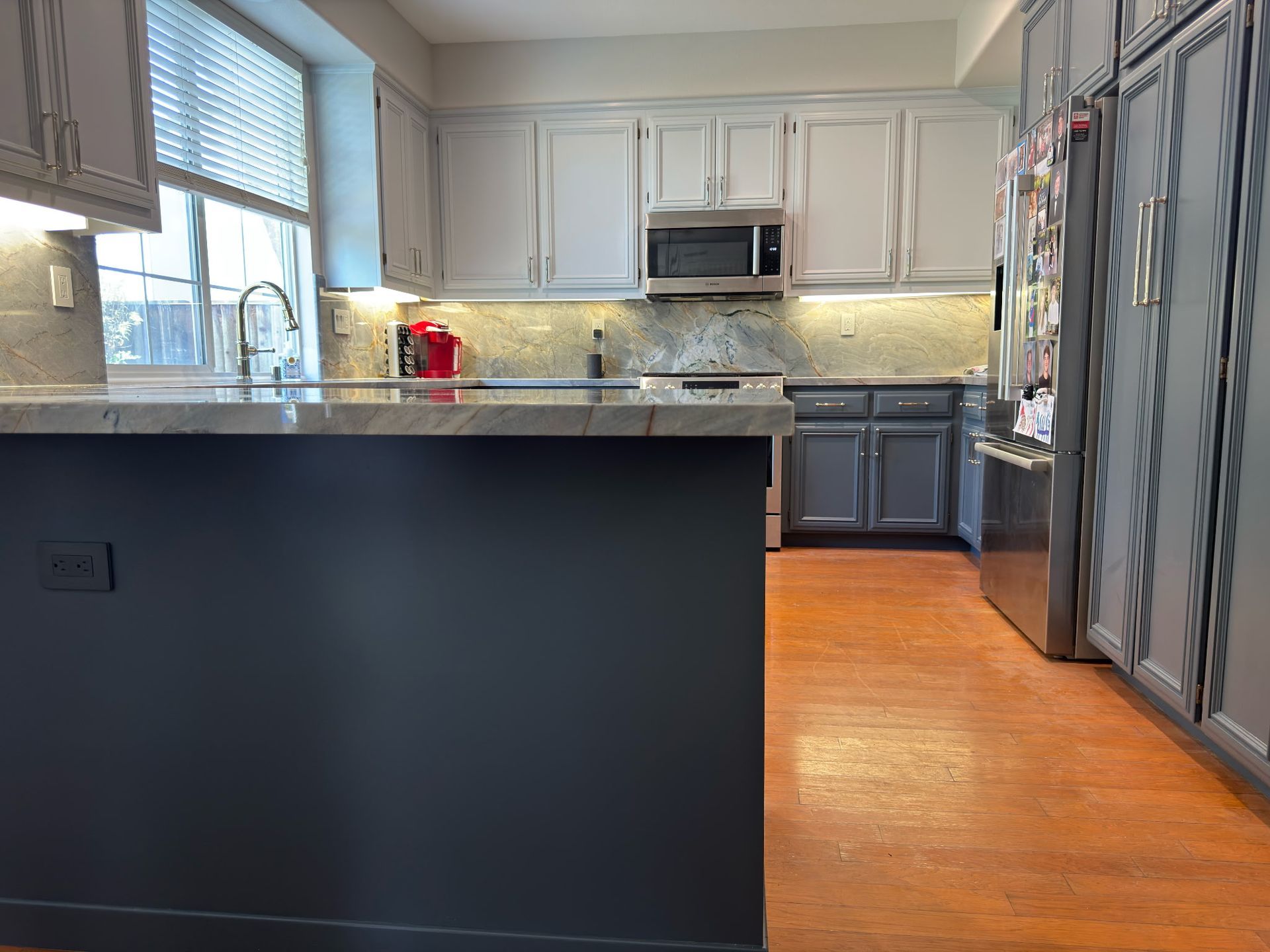 A modern kitchen featuring a dark gray island, white upper cabinets, gray lower cabinets, and light wood flooring.