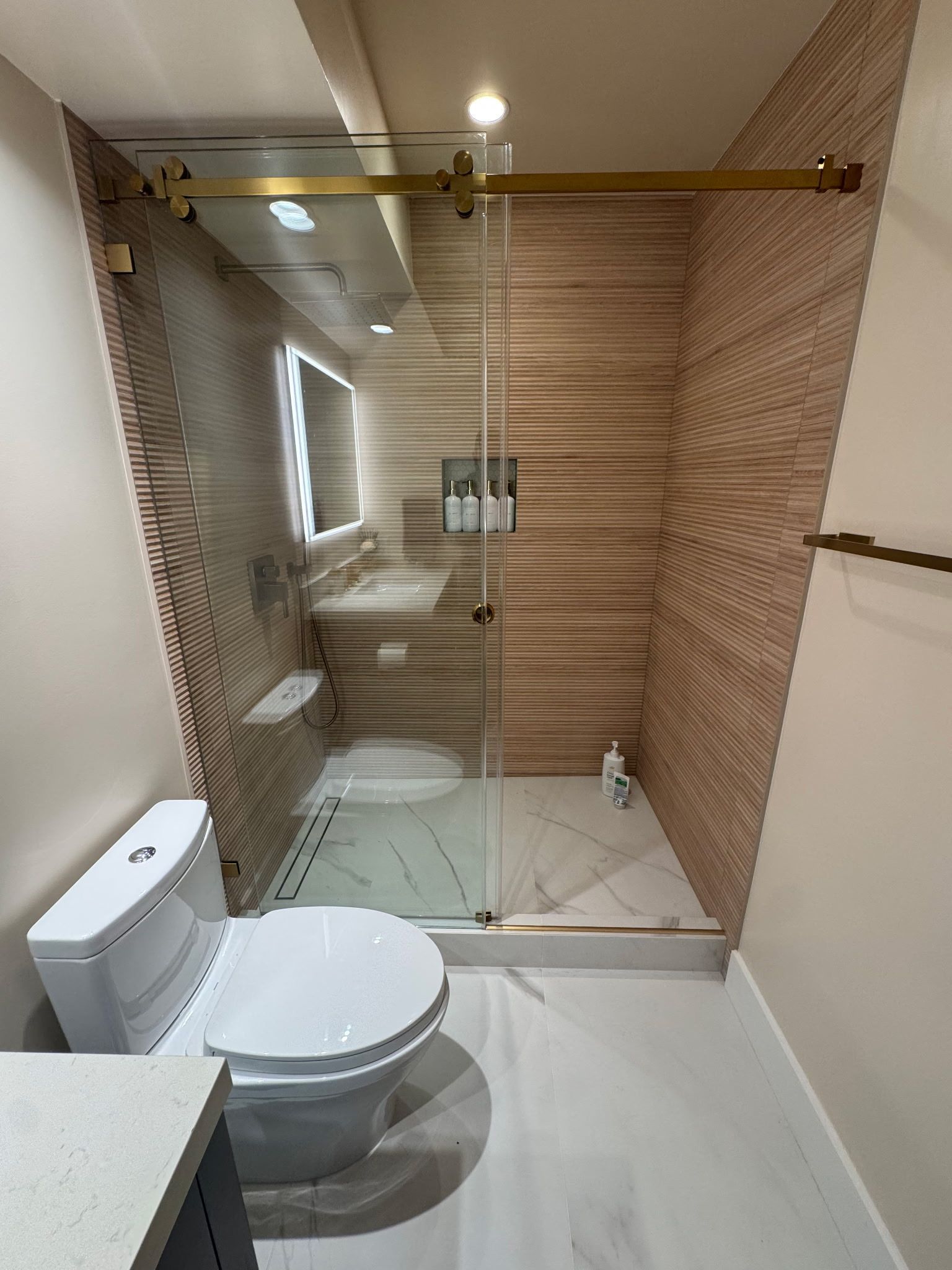 A modern, marble-tiled walk-in shower featuring a recessed niche, a white soaking tub, and a mosaic-tiled floor.