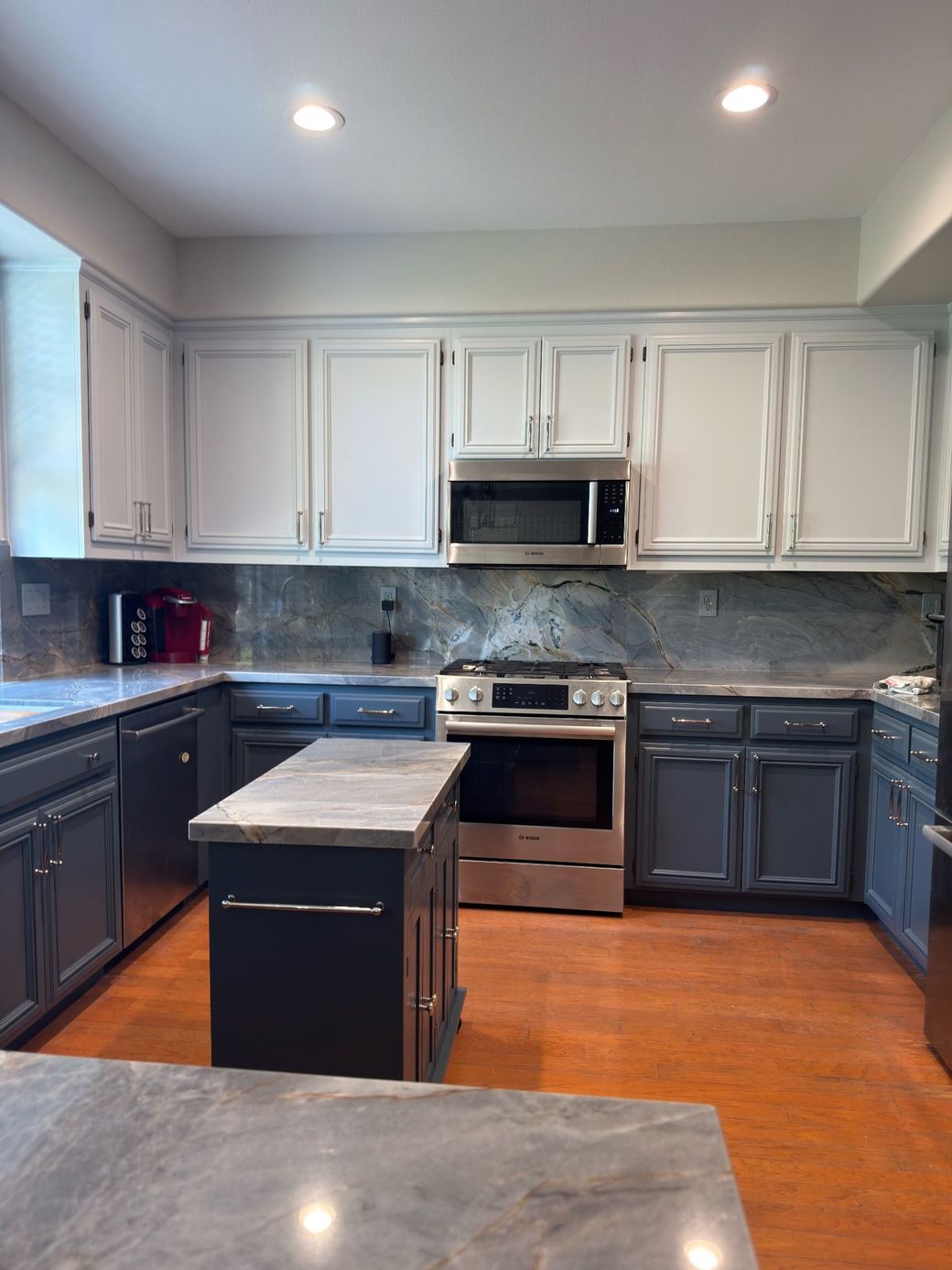A modern kitchen with a white marble island, dark cabinetry, and hanging pendant lights, leading to a dining area.
