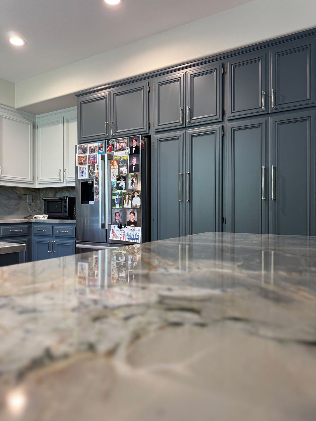 A modern kitchen featuring dark grey cabinets, a stainless steel refrigerator covered in magnets, and granite countertops. A modern kitchen featuring dark grey cabinets, a stainless steel refrigerator covered in magnets, and granite countertops.