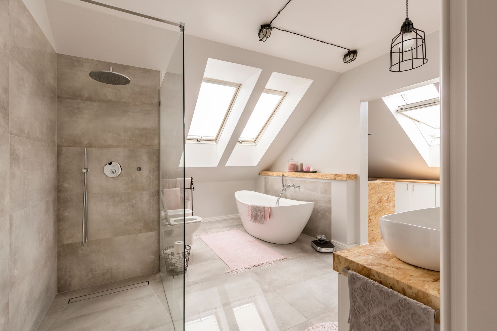 Modern attic bathroom featuring a glass-enclosed shower, a white freestanding bathtub, and a wood-topped vanity.