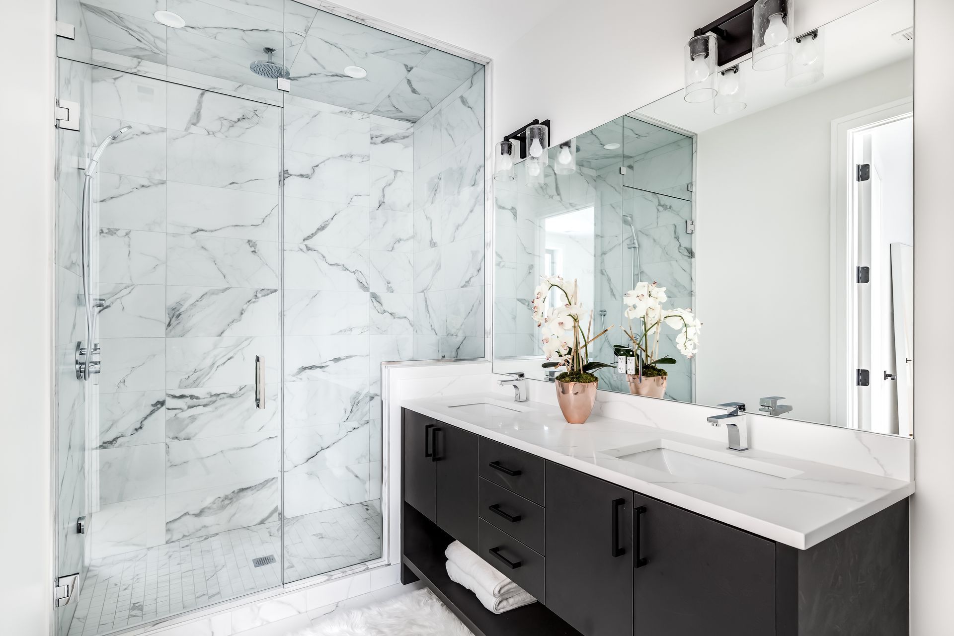 Modern bathroom with a glass-enclosed marble shower, black vanity cabinet, white countertop, and large wall mirror.