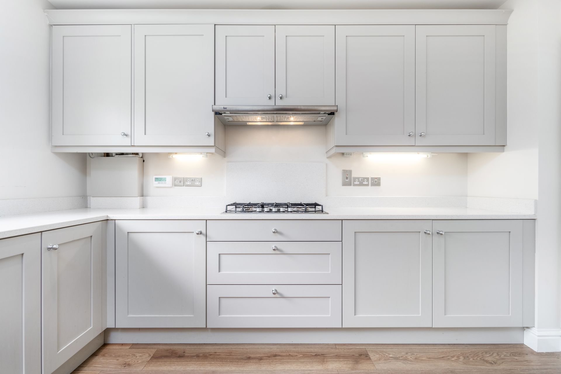 Modern light gray kitchen cabinets and drawers with white countertops and a gas stovetop, set against a white wall.