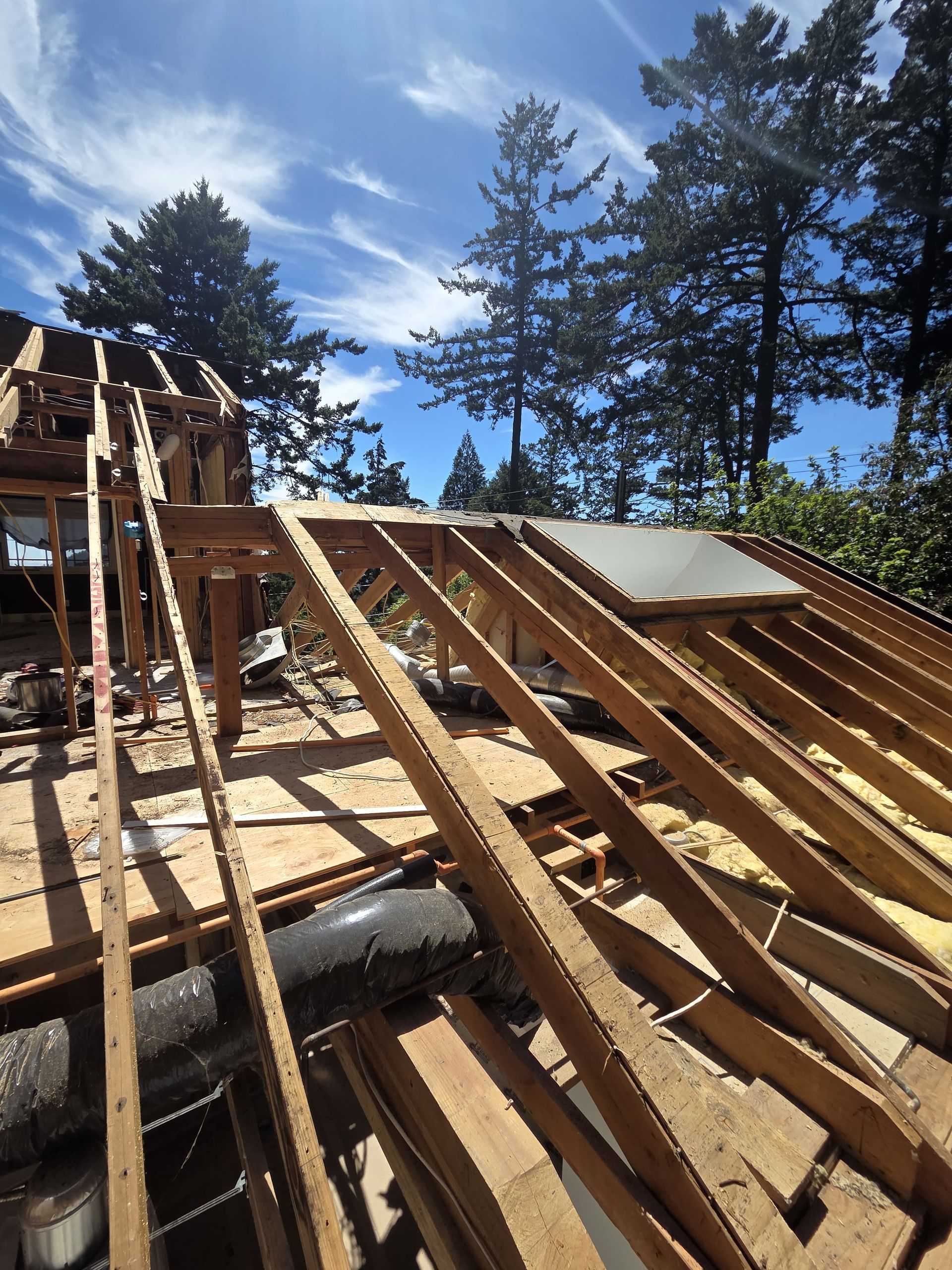 An interior view of a room under construction, showing wooden wall framing, exposed rafters, and a concrete floor.