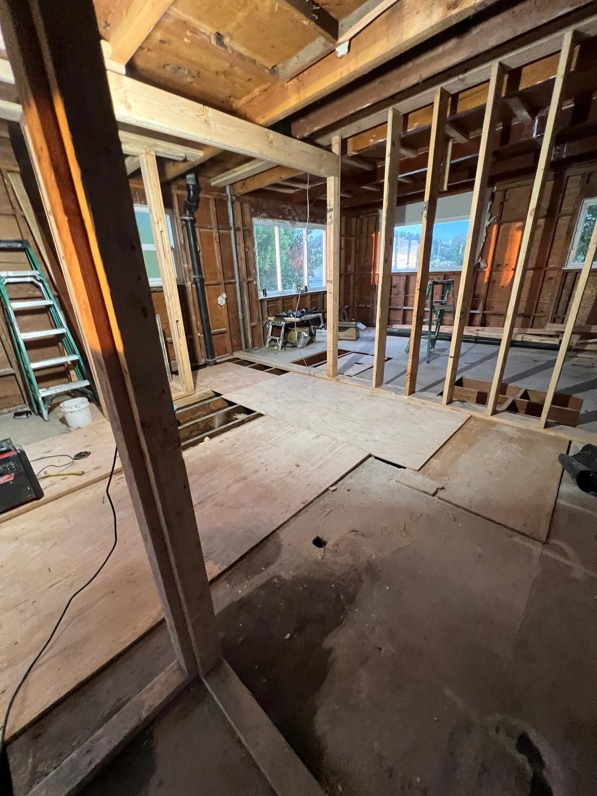 A sunlit room under construction with scaffolding, a ladder, bare concrete walls, and new wood flooring.