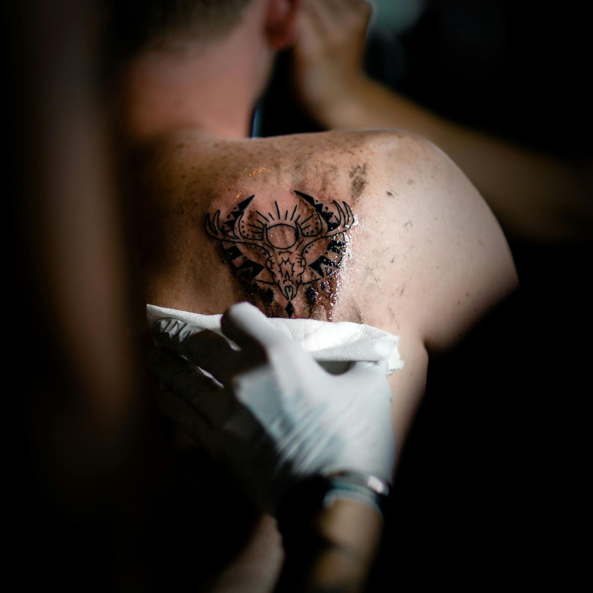 image of a gloved hand wiping excess ink away from a fresh tattoo on a man's shoulder