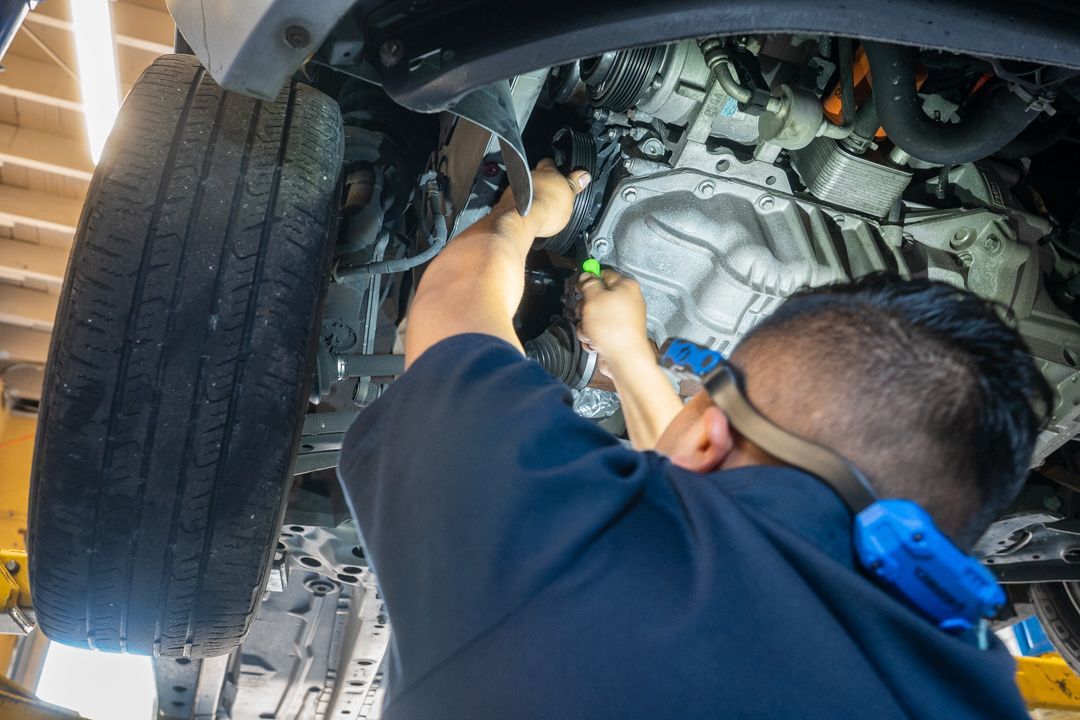 Mechanic working under a car, using a flashlight. Bright lighting. Close-up on the vehicle's underside.