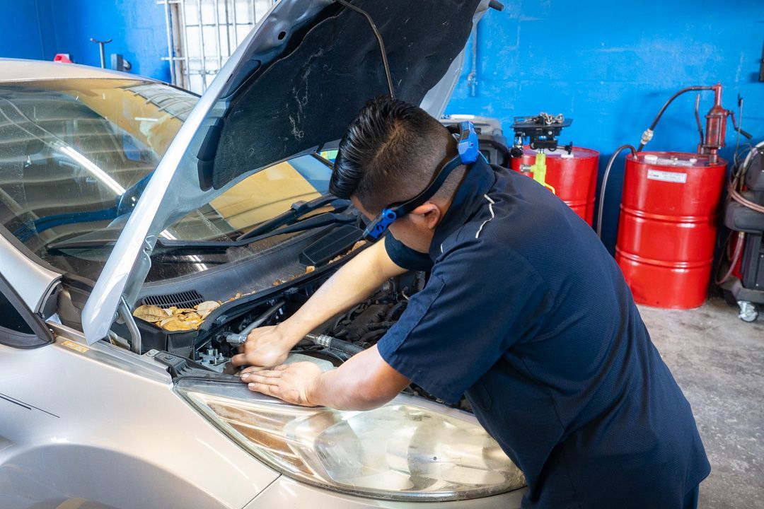 Mechanic in dark shirt and safety glasses working on a car engine in a garage.