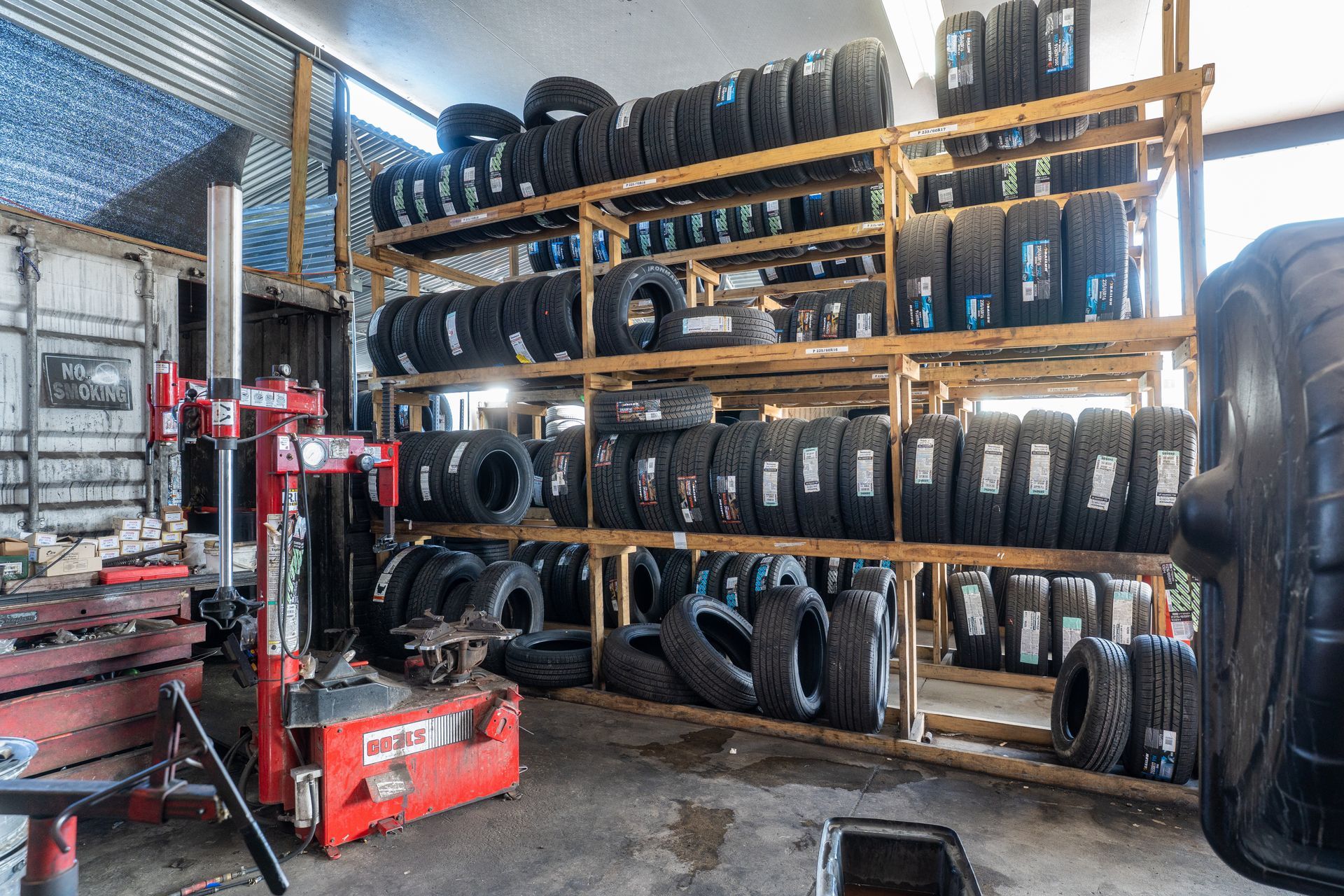 Tires stacked neatly on shelves in a garage. Black rubber with tread patterns.