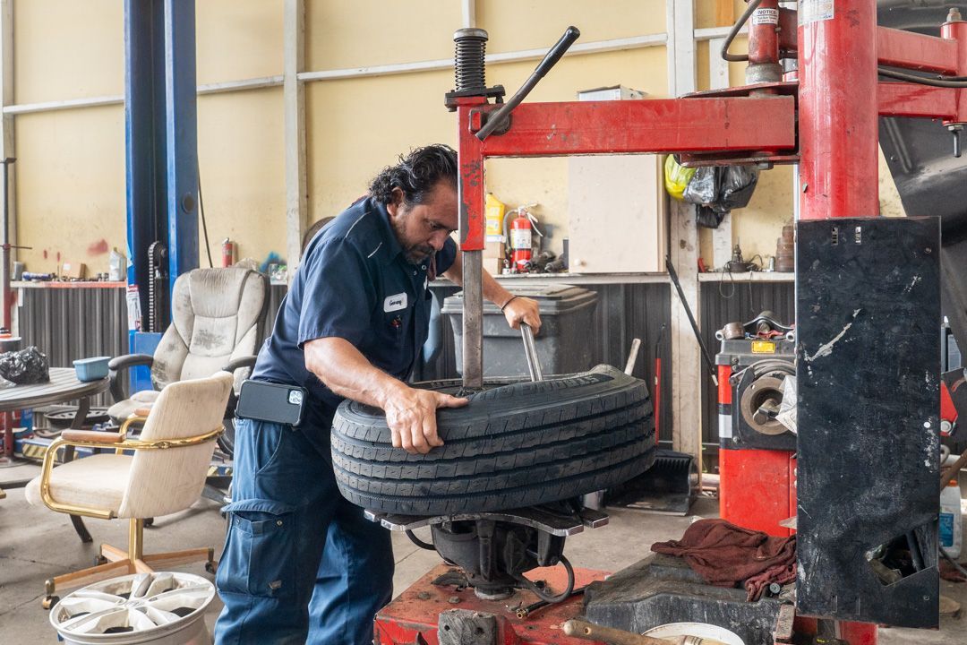 Mechanic using tire machine in auto shop, tire on the machine, working with a wrench.
