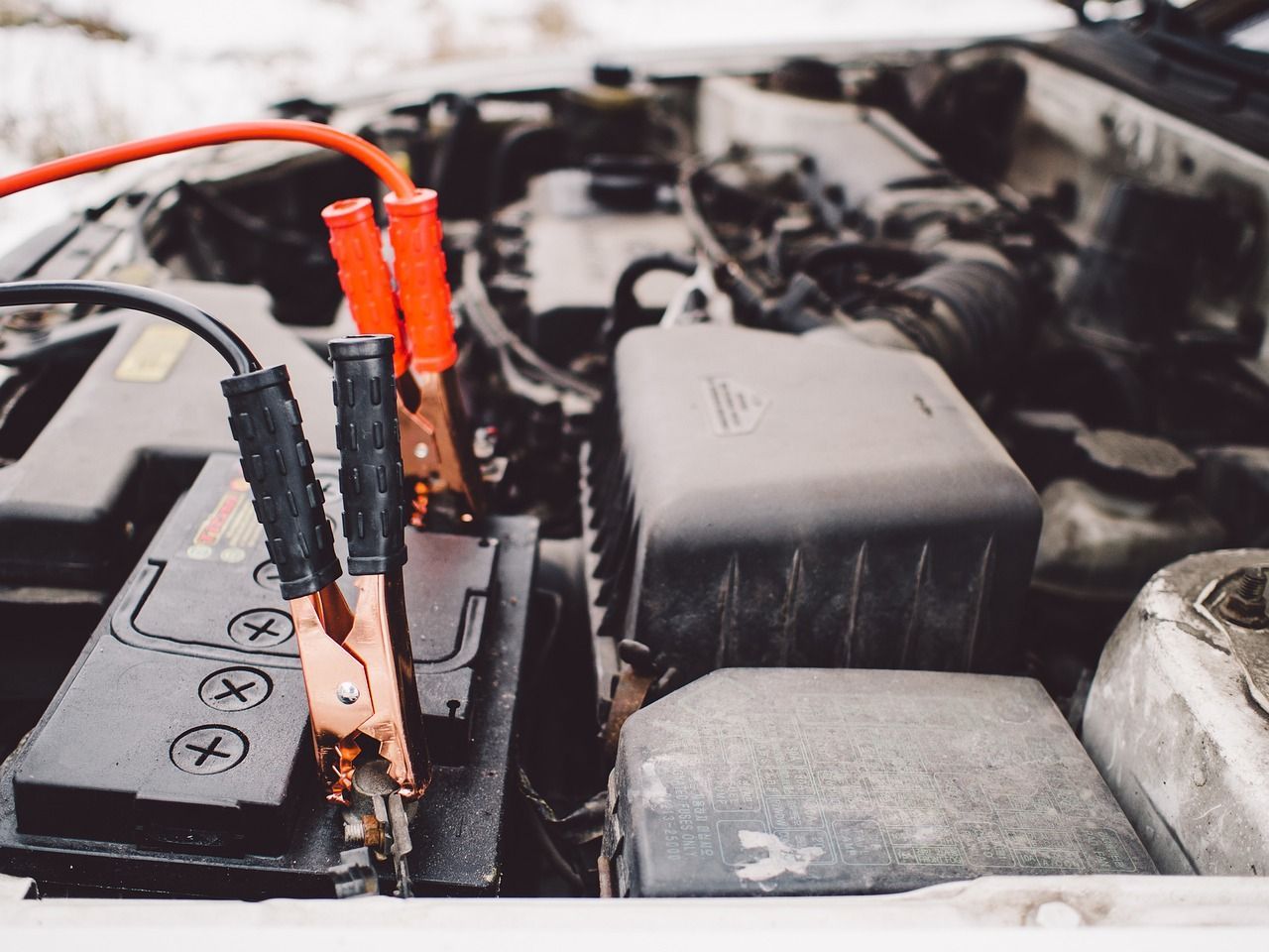 Alligator clips attached to a car battery in an engine bay