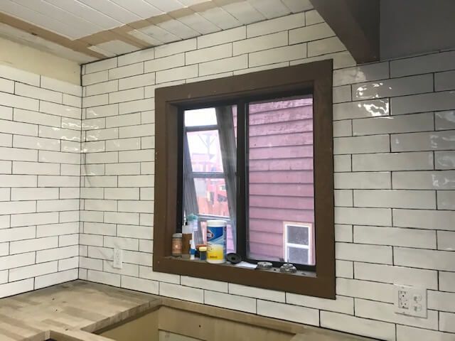 A kitchen with white tiles and a window with a wooden frame.