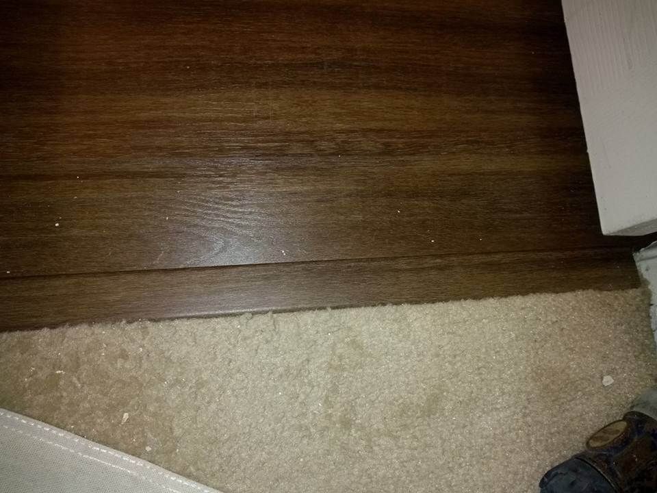 A person is standing on a wooden floor next to a carpet.