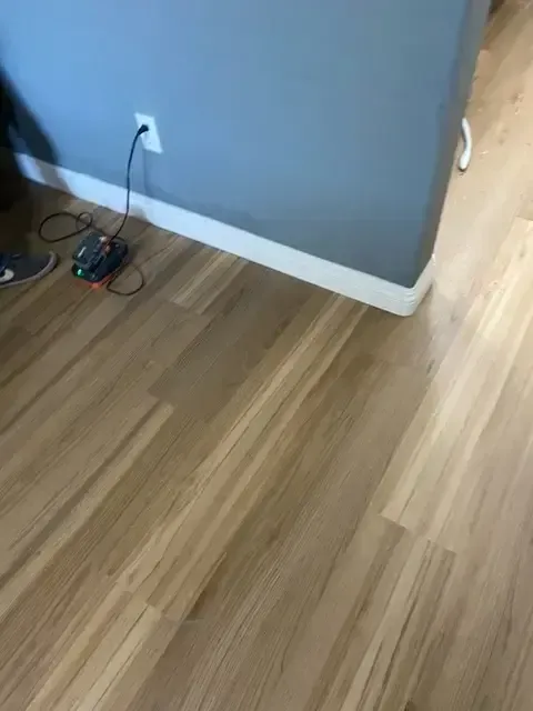 A person is standing on a wooden floor next to a wall.