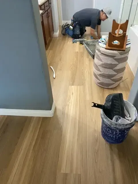 A man is kneeling on a wooden floor next to a trash can.