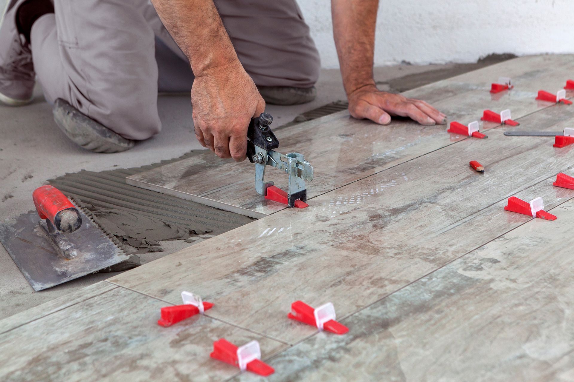 A man is kneeling on the floor tiling a floor.