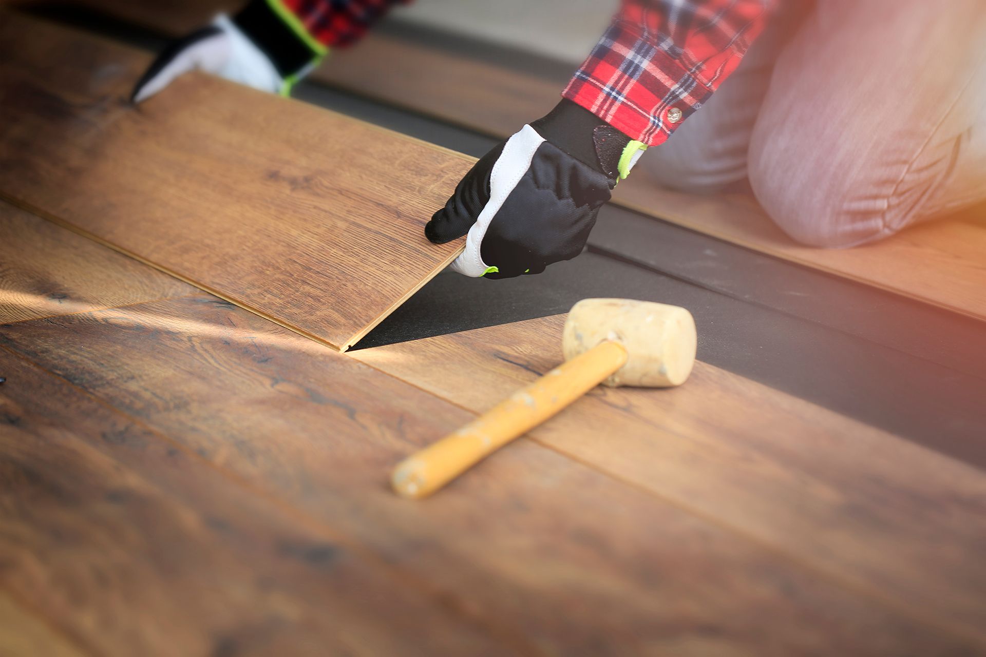 A person is installing a wooden floor with a hammer.