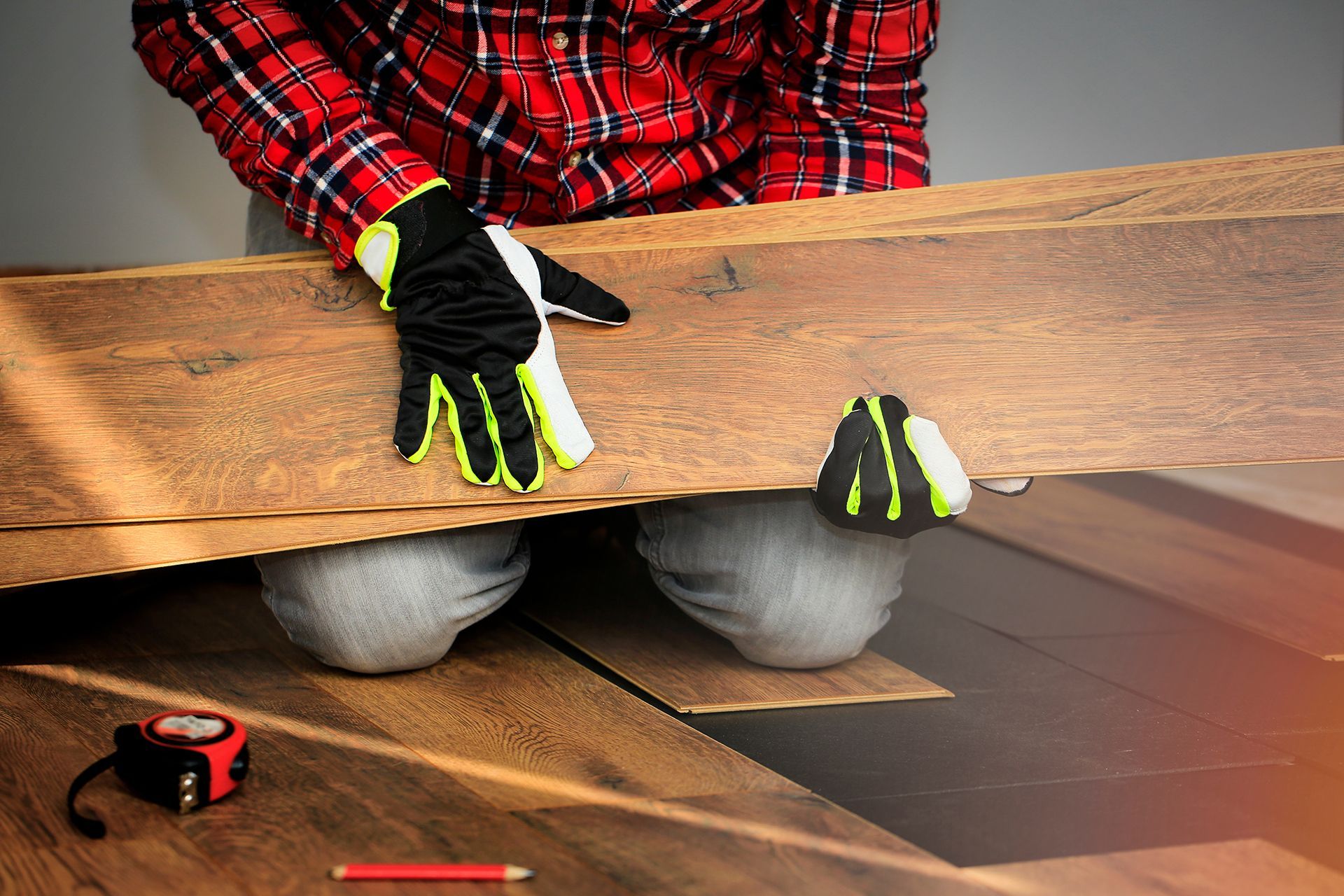 A man wearing gloves is installing a wooden floor.