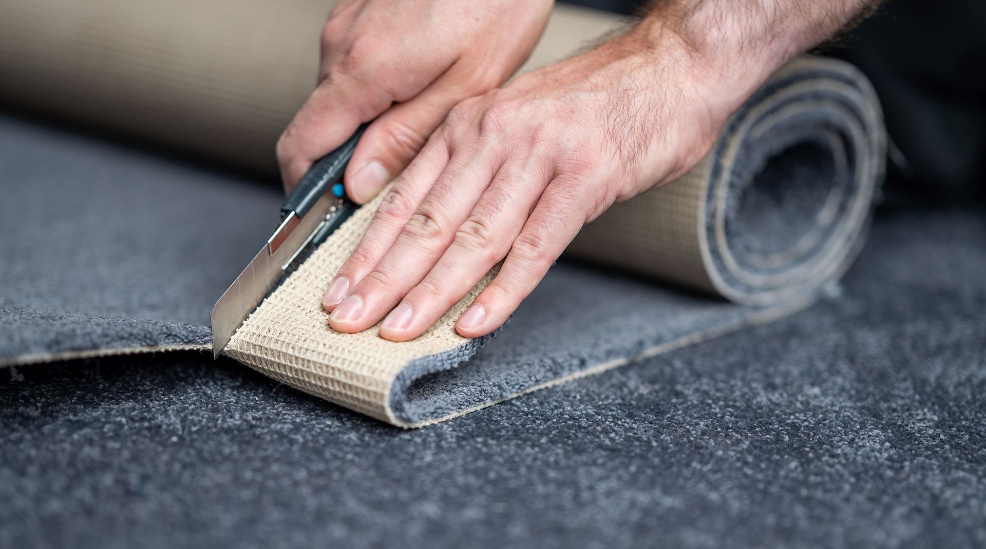 A man is cutting a roll of carpet with a pair of scissors.