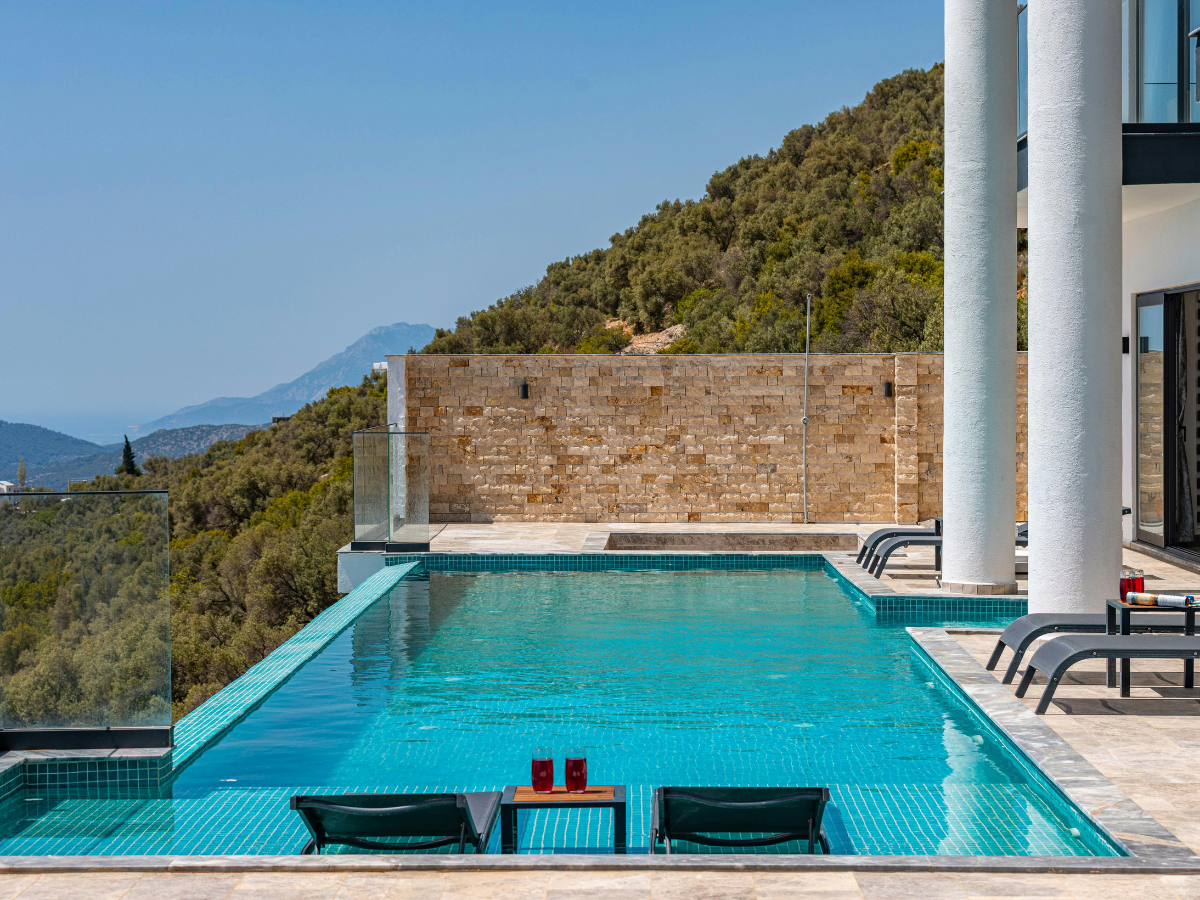 Infinity pool overlooking mountains and sea; sun loungers, blue water, sunny day.