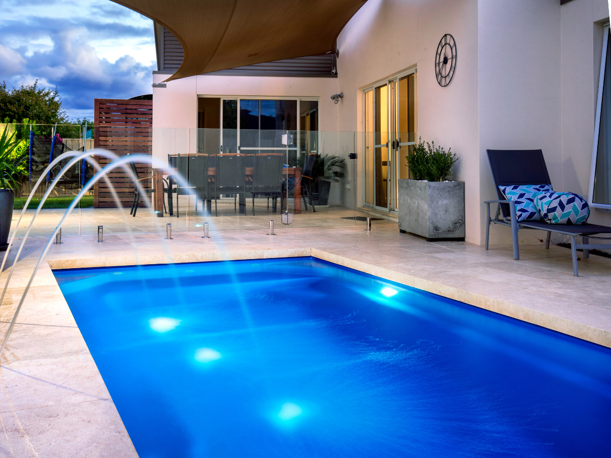 Outdoor pool with fountain, patio seating, and a sun shade.