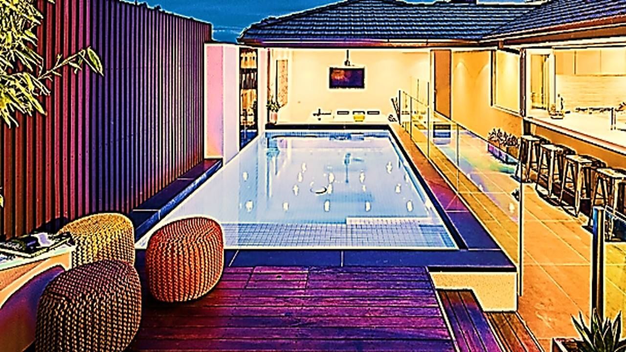 A rectangular pool in an outdoor setting at dusk. Includes wooden deck, seating, and a covered entertainment area.