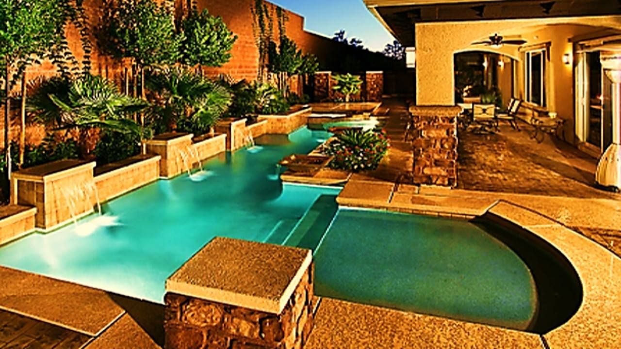 Luxury outdoor pool with cascading waterfalls, lit at dusk.